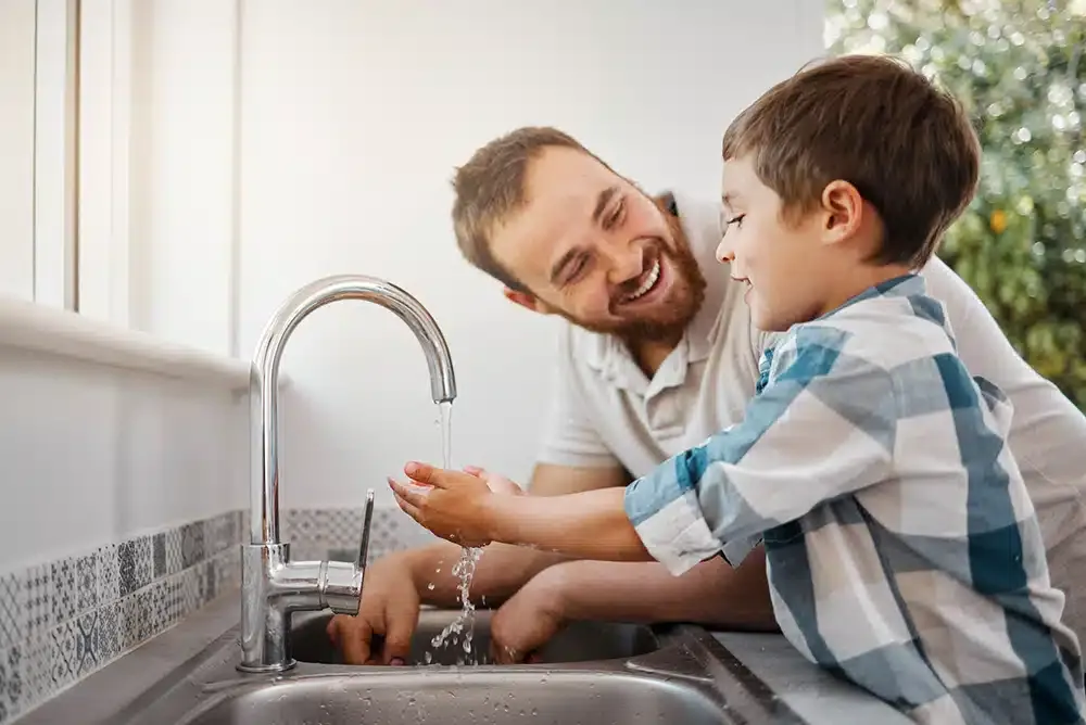Father helping son wash hands in kitchen sink in residential home in Hillsdale, NJ.
