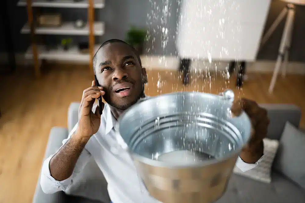 Water leaking from ceiling with man holding bucket on the phone in Hillsdale, NJ.